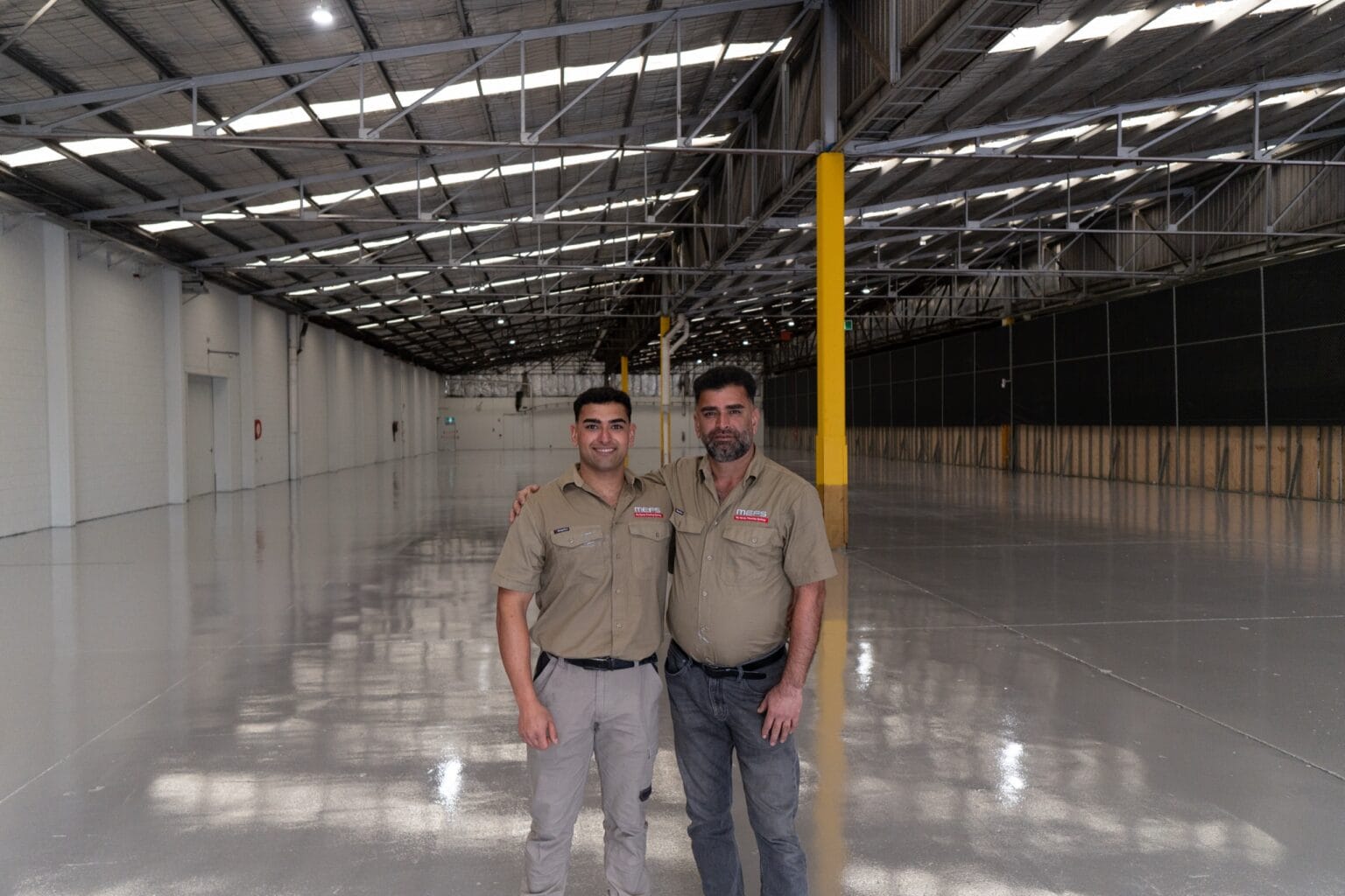 Sean and his dad in MEFS work shirts on a finished grey epoxy warehouse floor